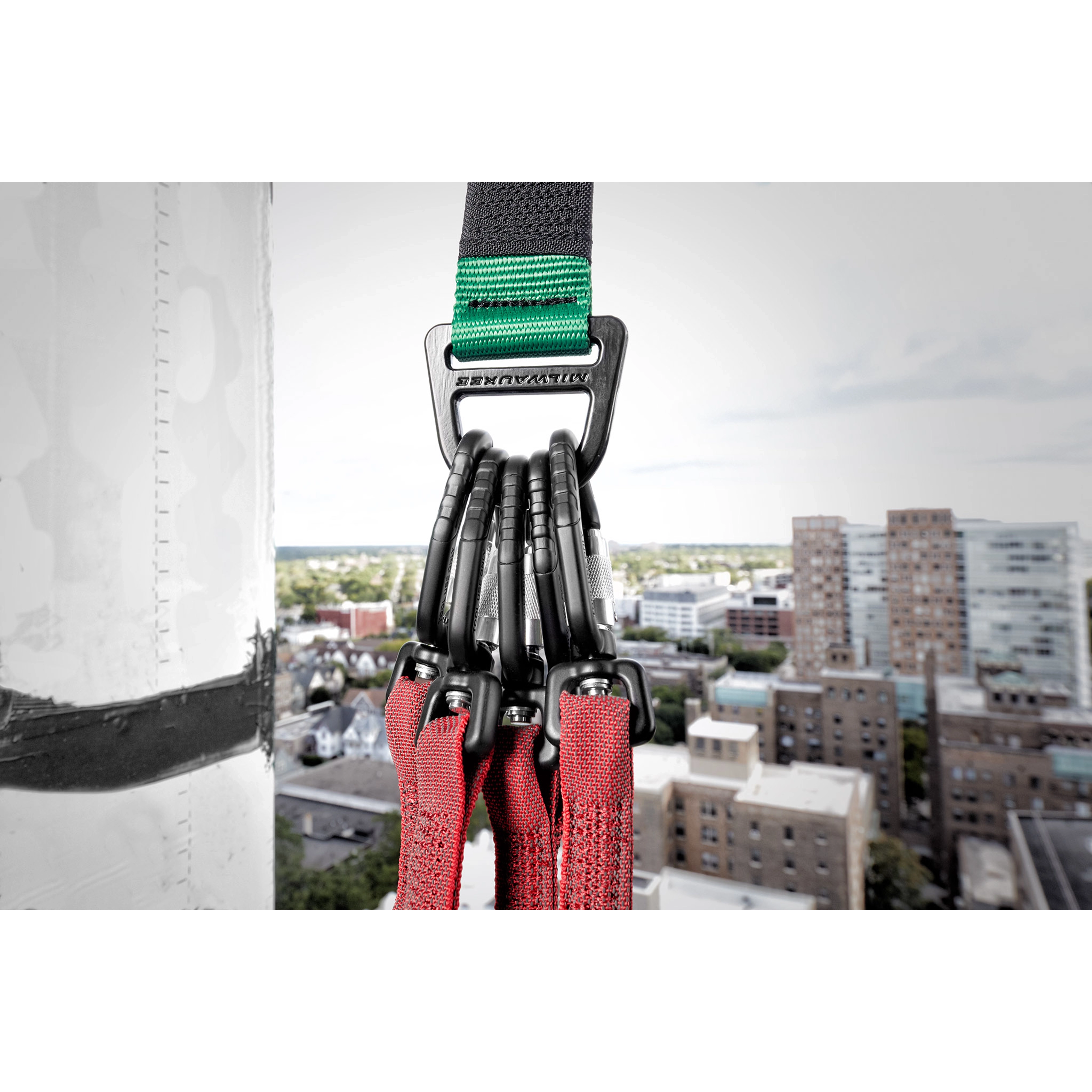 50LBS Anchor Strap with multiple carabiners attached to red straps, hanging from a high-rise building, cityscape in the background.