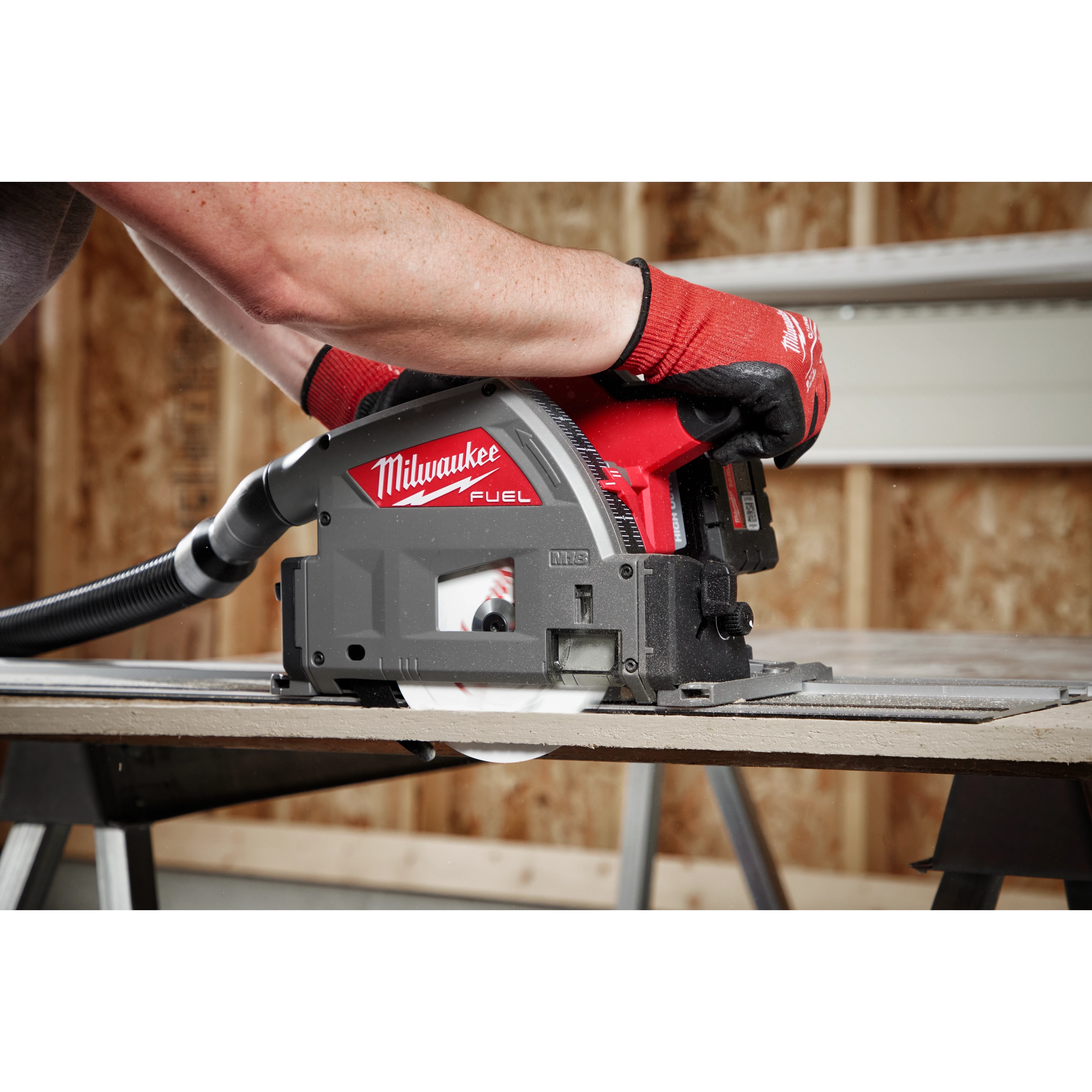 Milwaukee 6-1/2" 4T Fiber Cement Track Saw Blade being used by a person wearing red gloves to cut through fiber cement board.
