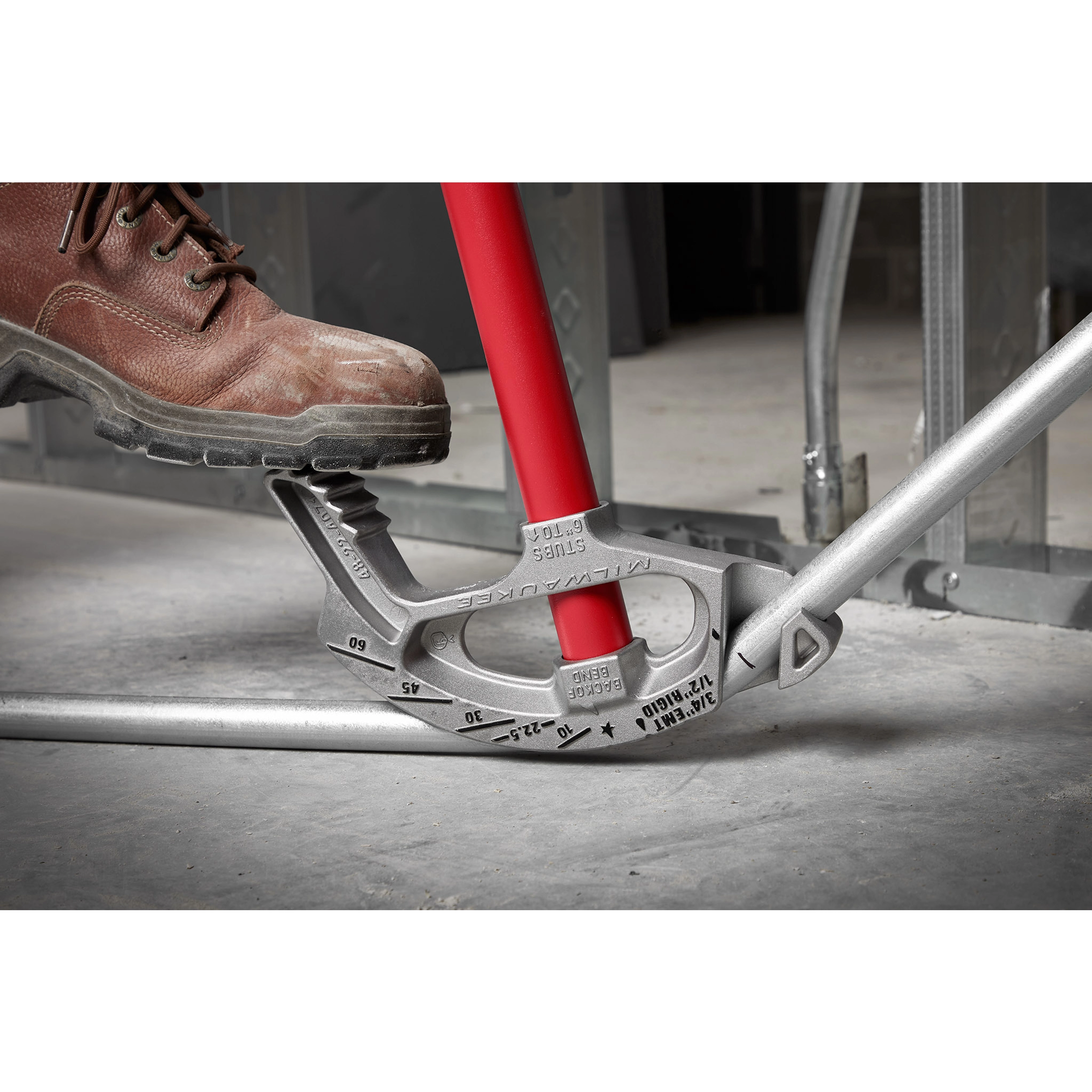 A foot pressing down on the 3/4" EMT Aluminum Conduit Bender with a red handle, bending a metal conduit pipe.