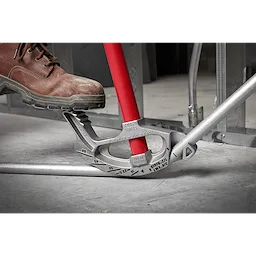 A foot pressing down on the 3/4" EMT Aluminum Conduit Bender with a red handle, bending a metal conduit pipe.