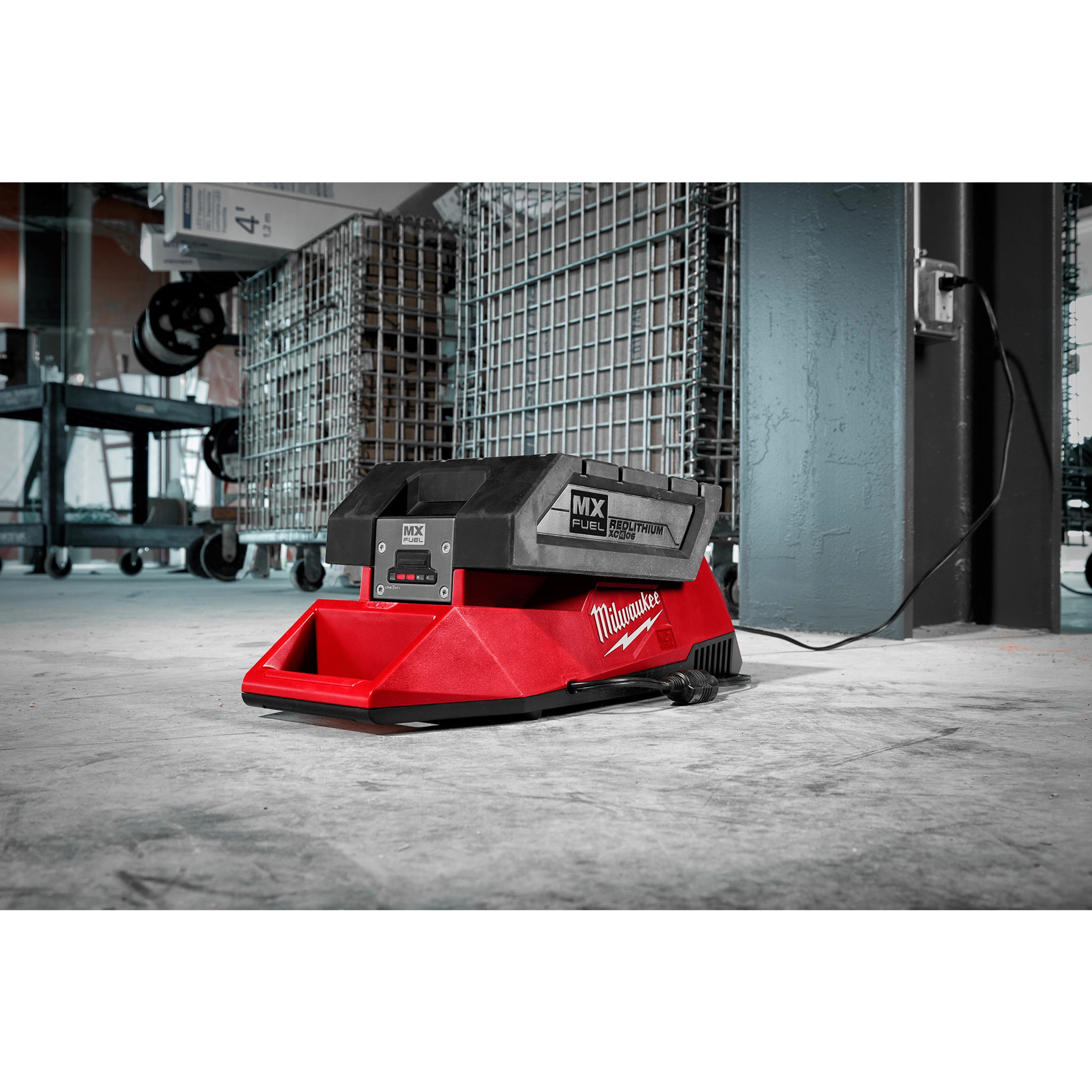 MX FUEL Charger in a workshop, placed on the floor, connected to a power outlet with industrial shelving units in the background.