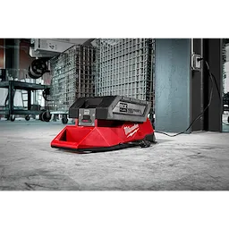 MX FUEL Charger in a workshop, placed on the floor, connected to a power outlet with industrial shelving units in the background.