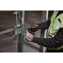 A person wearing safety gloves uses a 10-24 AWG Adjustable Compact Wire Stripper & Cutter to strip electrical wires attached to a metal frame.