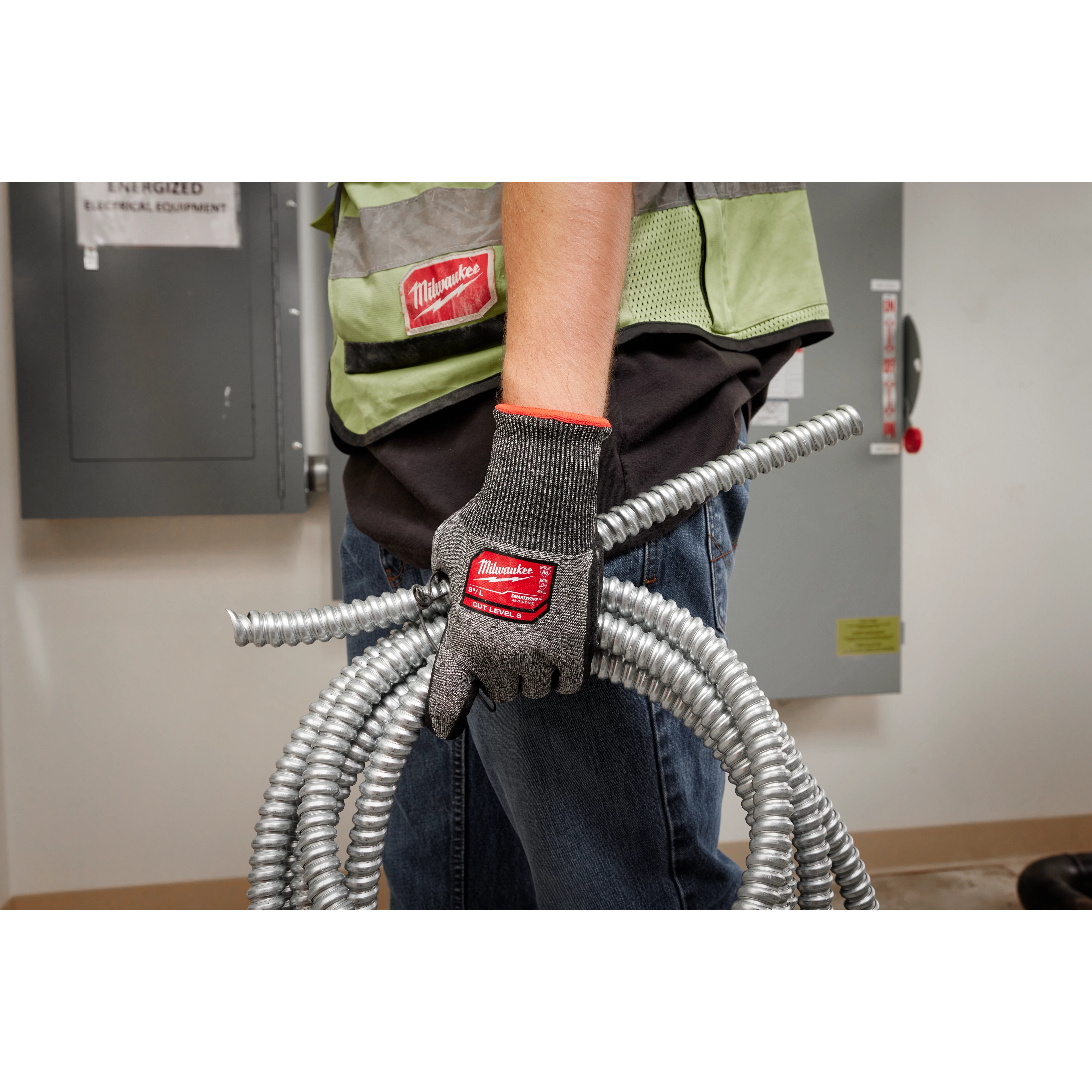 Person wearing Cut Level 5 High-Dexterity Nitrile Dipped Gloves - L, holding coiled metal conduits in a workshop.