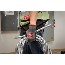 Person wearing Cut Level 5 High-Dexterity Nitrile Dipped Gloves - L, holding coiled metal conduits in a workshop.