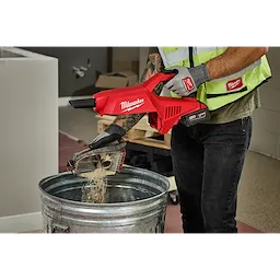 A person is emptying dust from the M18 Brushless Handheld Vacuum into a metal trash can.