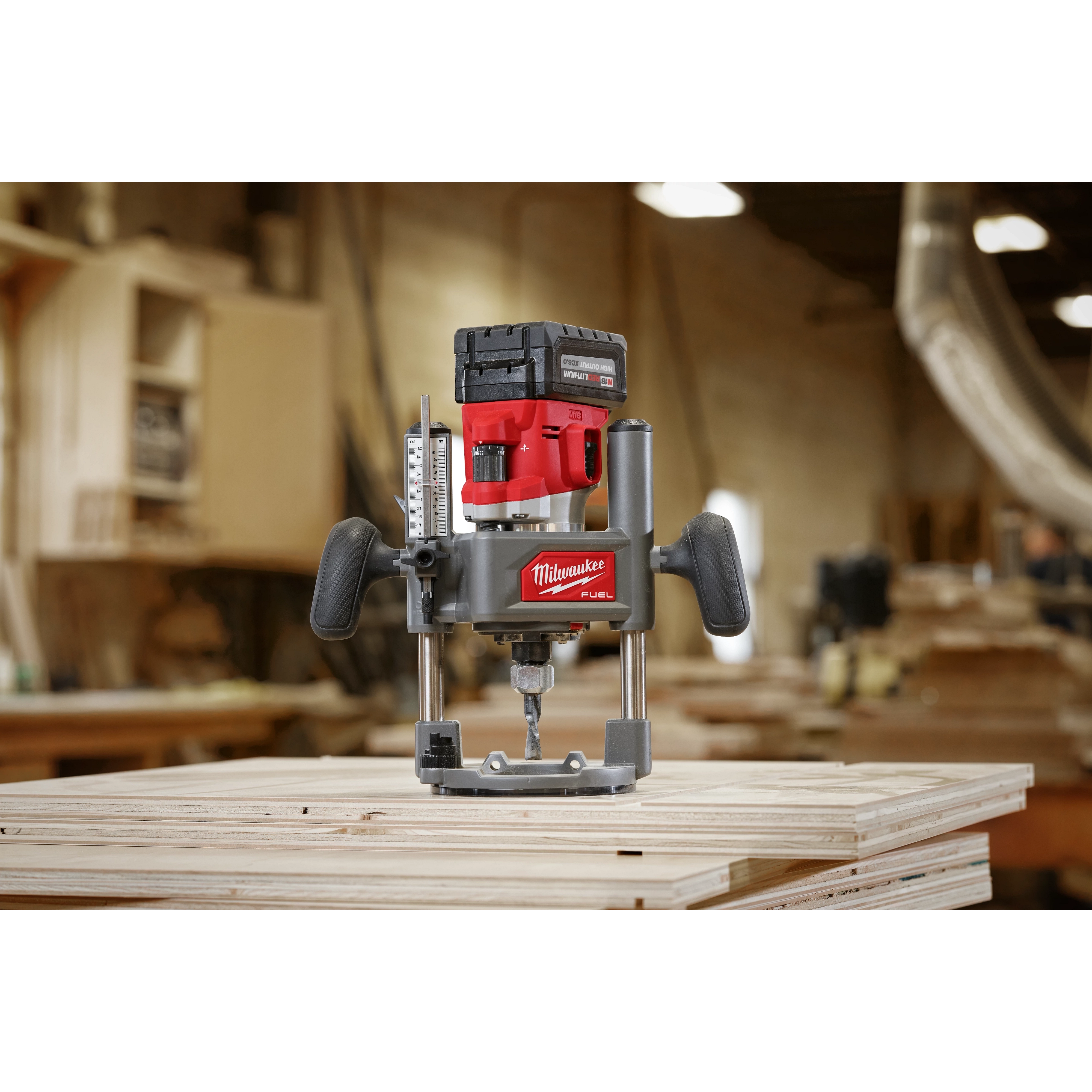 M18 FUEL 1/2" Router placed on stacked plywood sheets in a workshop, featuring ergonomic handles and a cordless battery system.