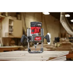 M18 FUEL 1/2" Router placed on stacked plywood sheets in a workshop, featuring ergonomic handles and a cordless battery system.