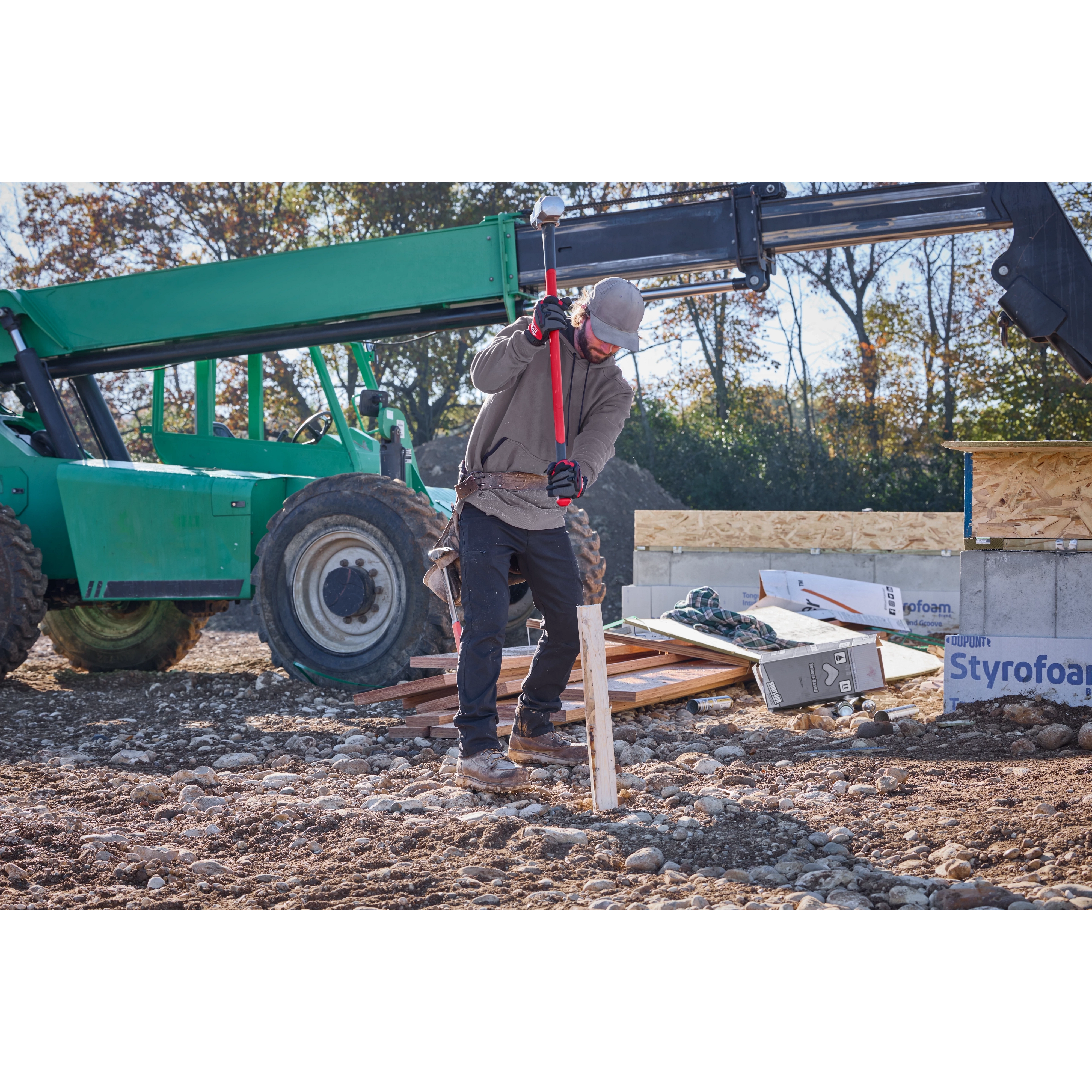 A construction worker using a 10lb Sledge Hammer (34" Handle) to drive a wooden stake into the ground at a building site.