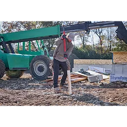 A construction worker using a 10lb Sledge Hammer (34" Handle) to drive a wooden stake into the ground at a building site.