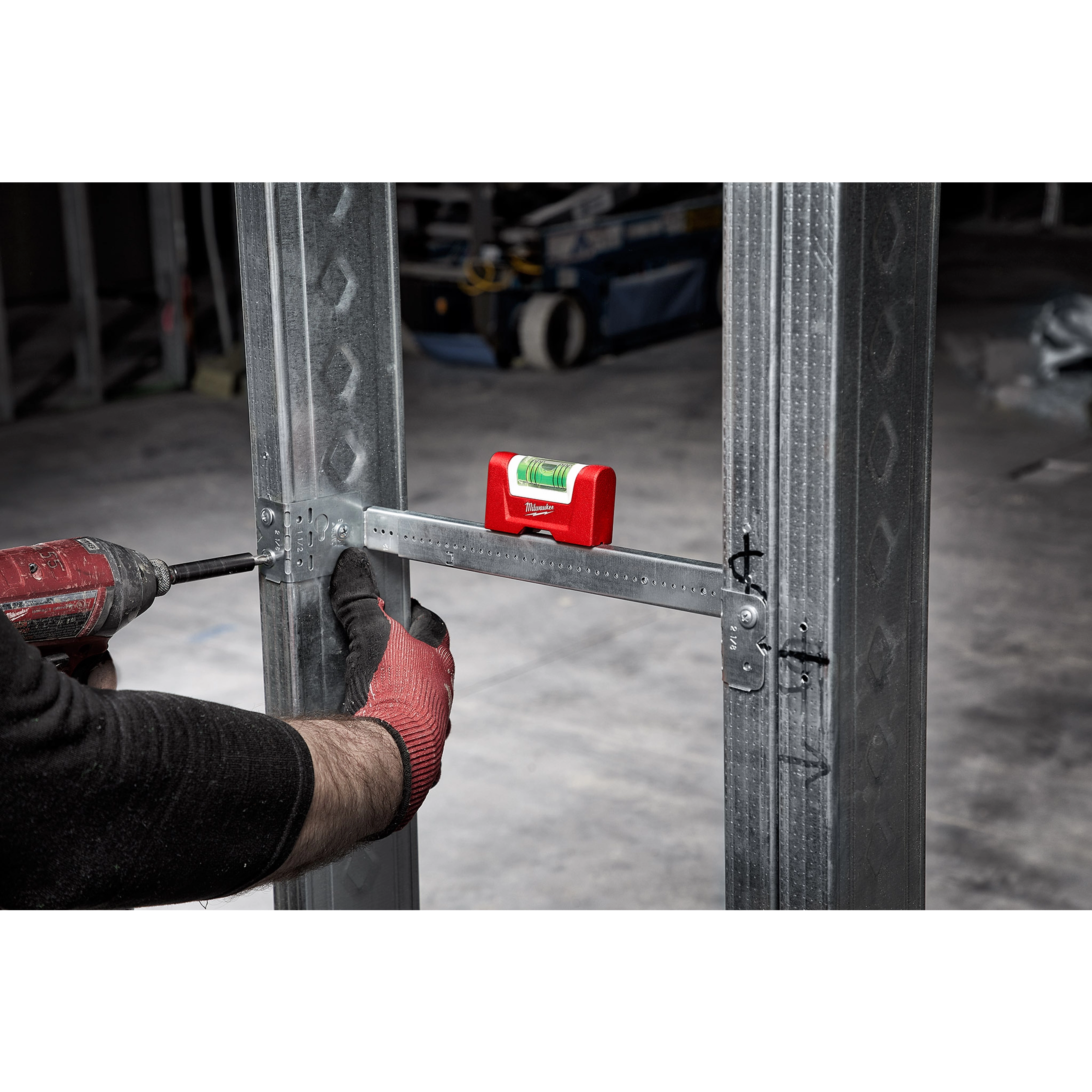 Construction worker using a red Pocket Level to ensure proper alignment of a metal frame, with a drill in the other hand.
