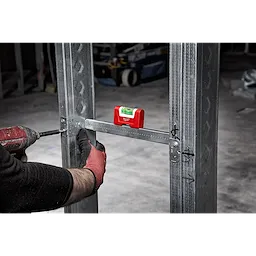 Construction worker using a red Pocket Level to ensure proper alignment of a metal frame, with a drill in the other hand.