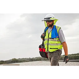 A construction worker wearing a high-visibility vest and a white hard hat carries a bag with a blue Cooling Towel around his neck.