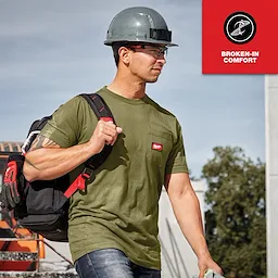 Man wearing hard hat and carrying tools in a green GRIDIRON Pocket T-Shirt - Short Sleeve with a red patch on the chest.