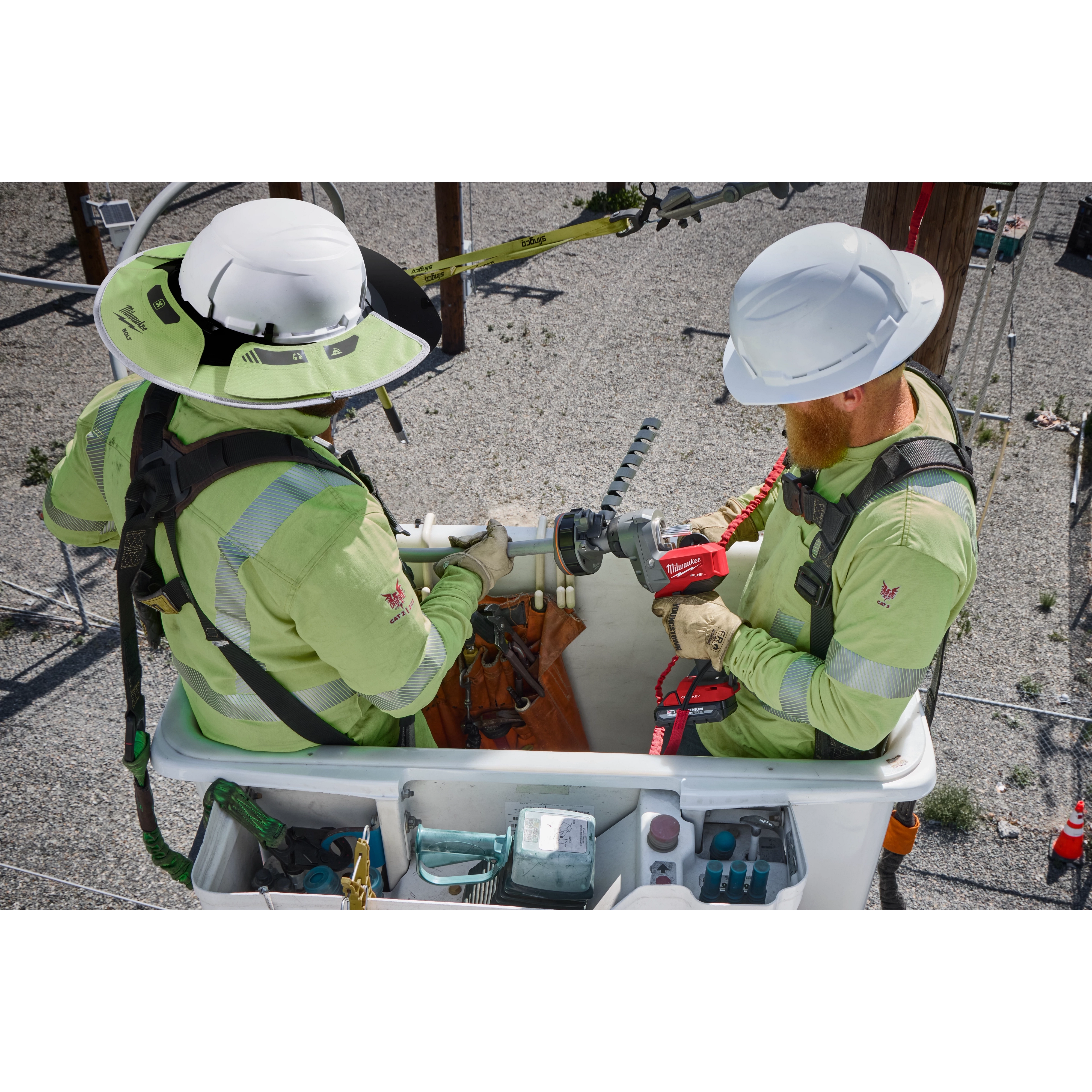 Utility workers using a Milwaukee M18 FUEL utility cable stripping tool on power lines atop a bucket truck. The image showcases its application in electrical utility maintenance, with additional tools and safety equipment visible in the bucket.