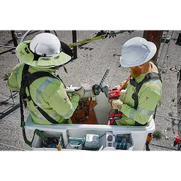 Utility workers using a Milwaukee M18 FUEL utility cable stripping tool on power lines atop a bucket truck. The image showcases its application in electrical utility maintenance, with additional tools and safety equipment visible in the bucket.