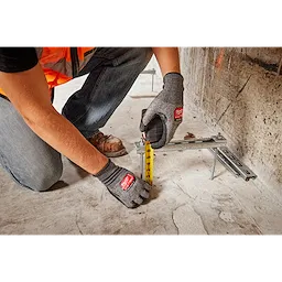 Person wearing Cut Level 3 High-Dexterity Nitrile Dipped Gloves - XL measures with a yellow tape measure on a construction site.