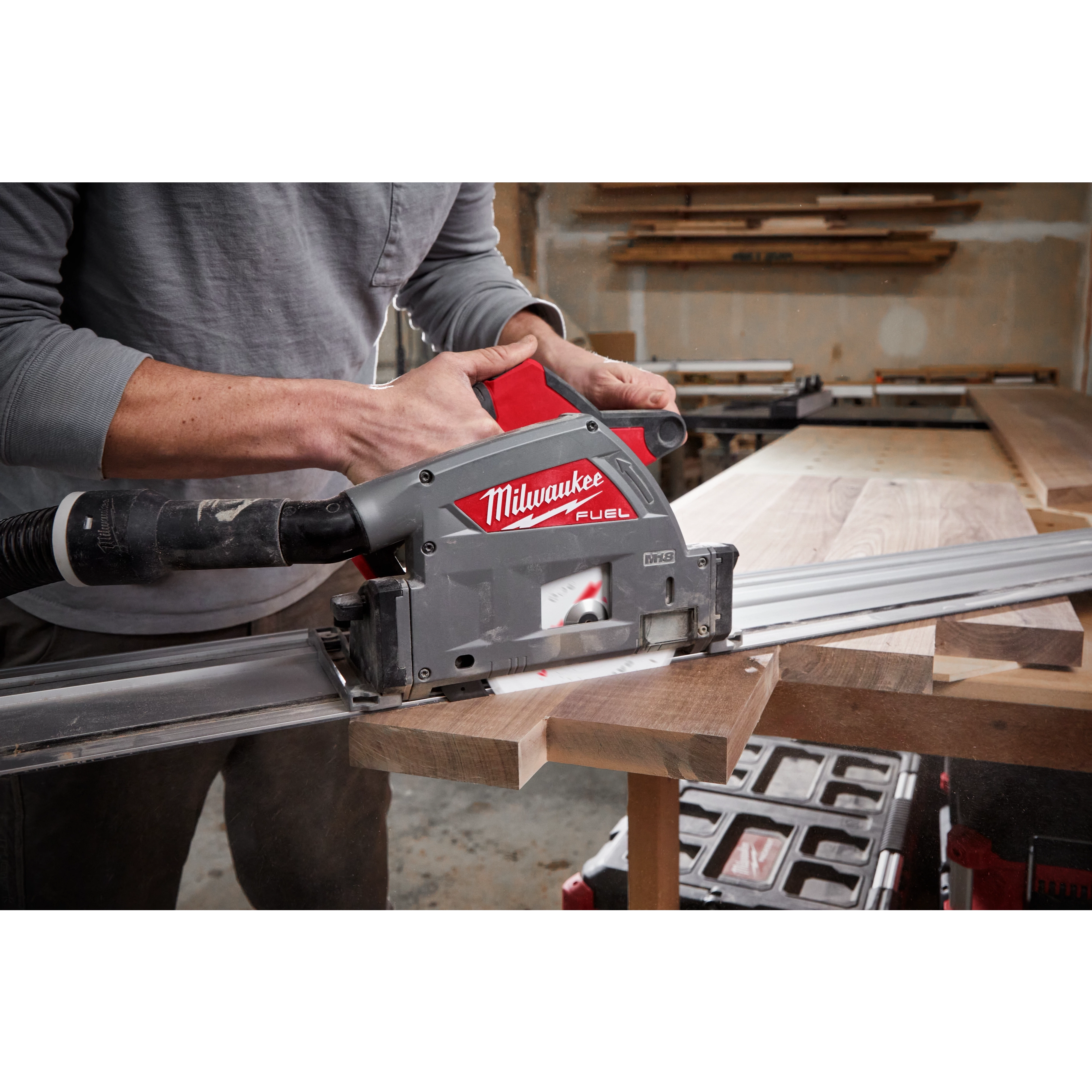 Person using a Milwaukee M18 FUEL 6 1/2" Plunge Track Saw to cut a piece of wood in a workshop setting.