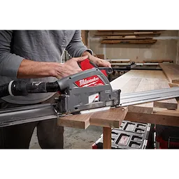 Person using a Milwaukee M18 FUEL 6 1/2" Plunge Track Saw to cut a piece of wood in a workshop setting.