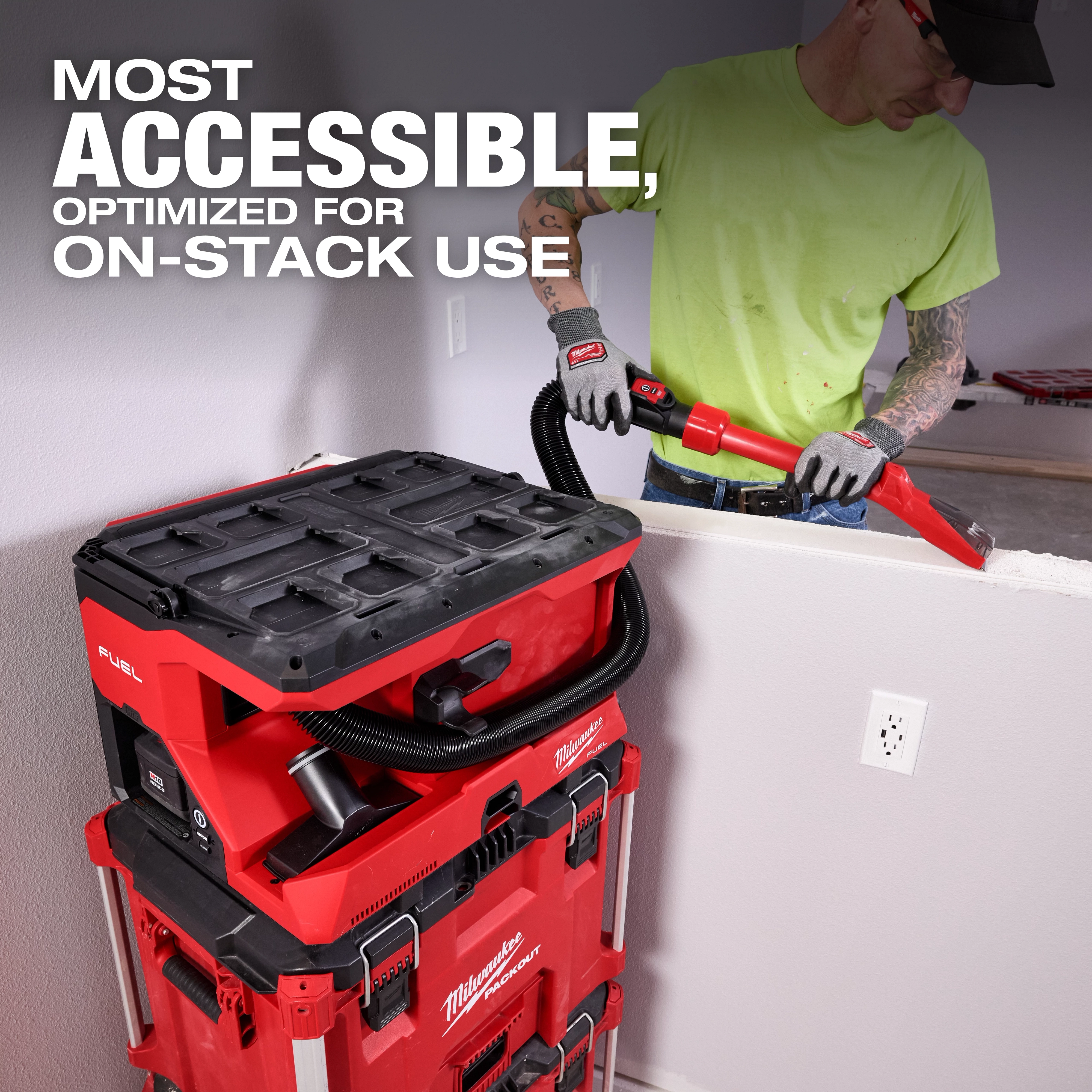 Worker using M18 FUEL 4 Gallon Wet/Dry Vacuum w/ PACKOUT Compatibility & VACLINK on stacked tool boxes near a wall.
