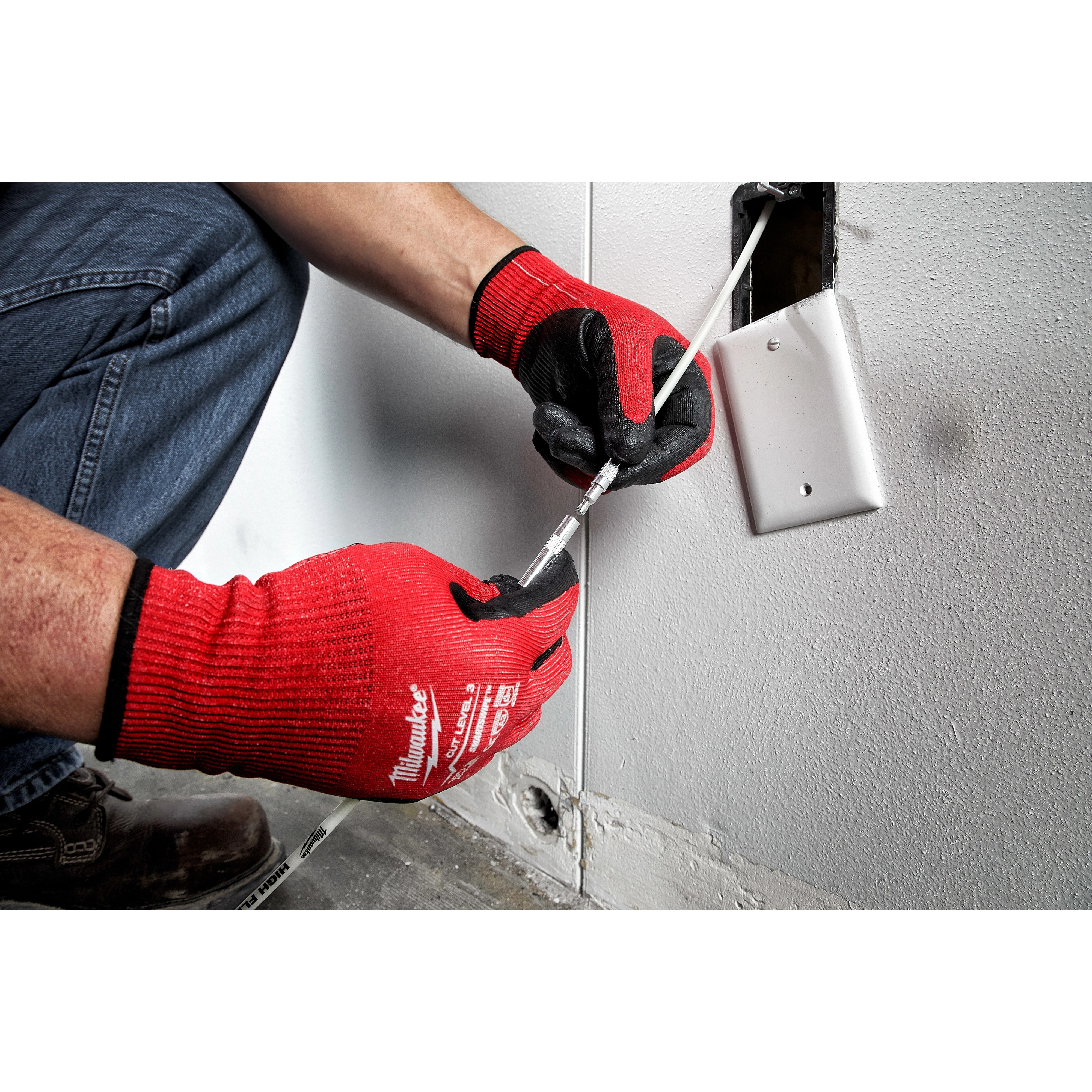 Person wearing red gloves using the 5' High Flex Fish Stick to install wiring through a wall outlet opening.