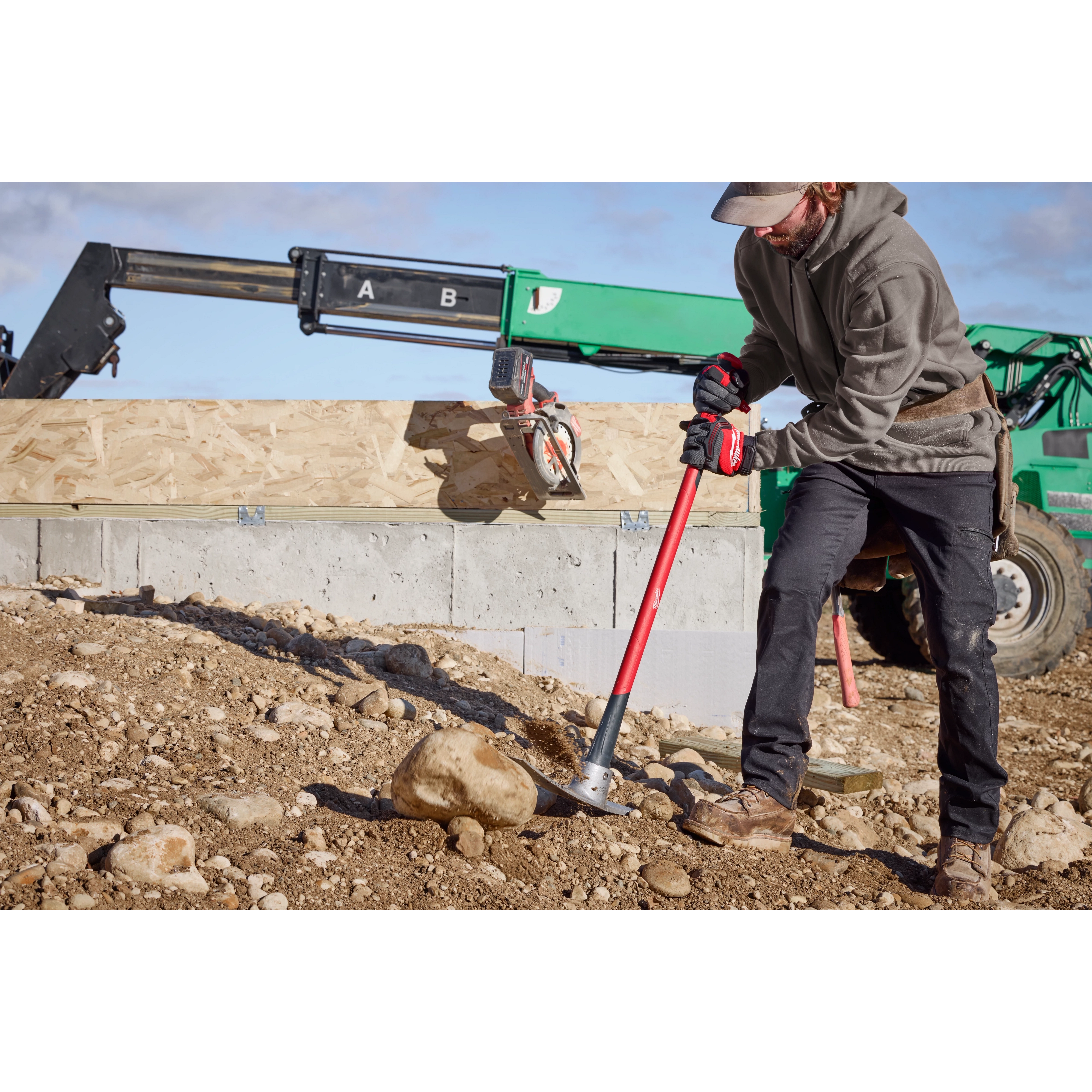 Man wearing work gloves and boots using 5lb Pick Mattock (36" Handle) to break up rocky soil on construction site.