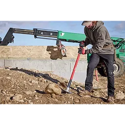Man wearing work gloves and boots using 5lb Pick Mattock (36" Handle) to break up rocky soil on construction site.