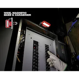 A REDLITHIUM USB ROVER Pivoting Flood Light is mounted above an electrical panel, illuminating it as a gloved hand works.