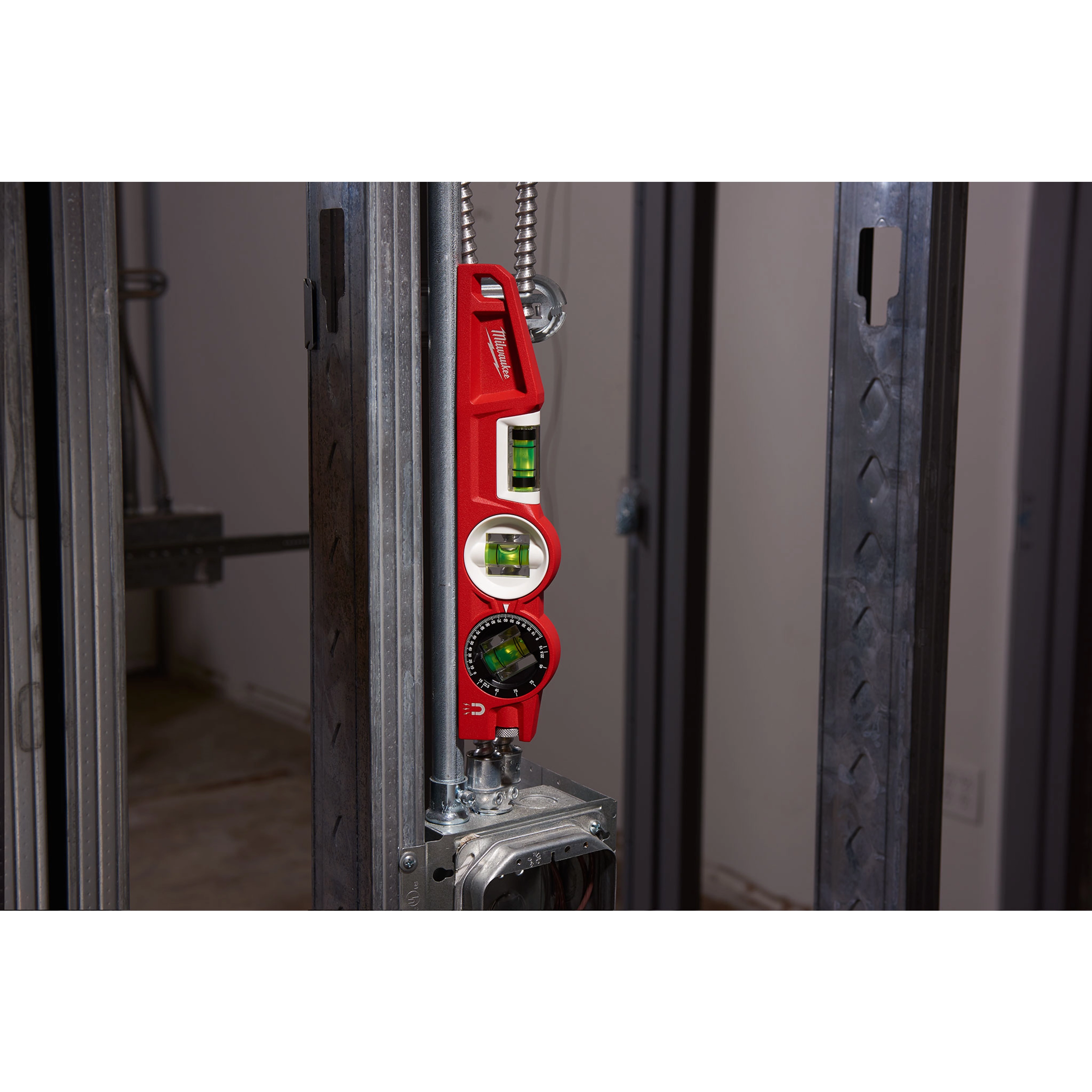 Red Block Torpedo Level attached to steel framing in a construction setting, showing three green vials for angle measurement.
