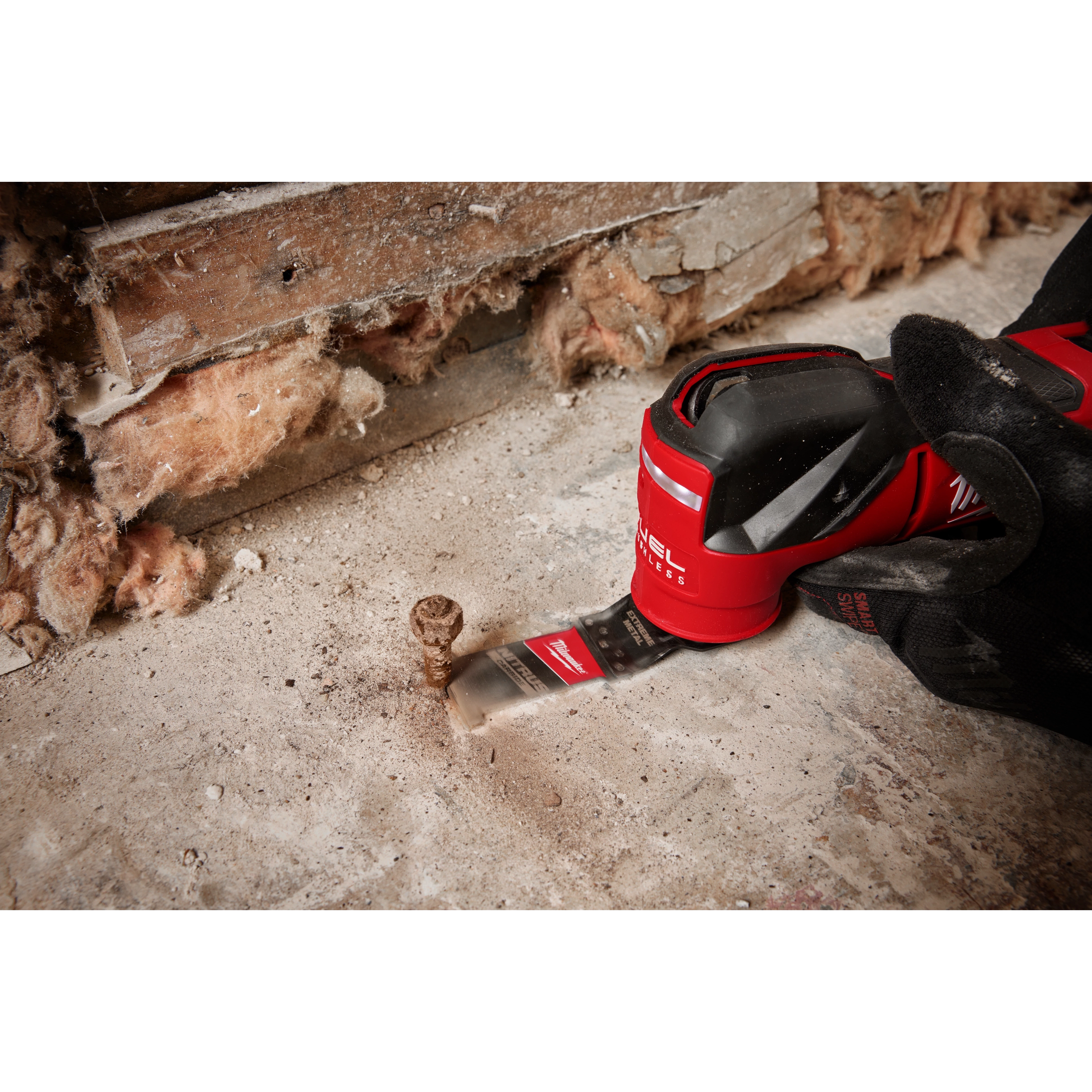 The NITRUS CARBIDE™ Extreme Metal Universal Fit OPEN-LOK™ Multi-Tool Blade is shown attached to a power tool, cutting a rusty bolt protruding from a concrete floor. The background includes exposed insulation and wooden beams.
