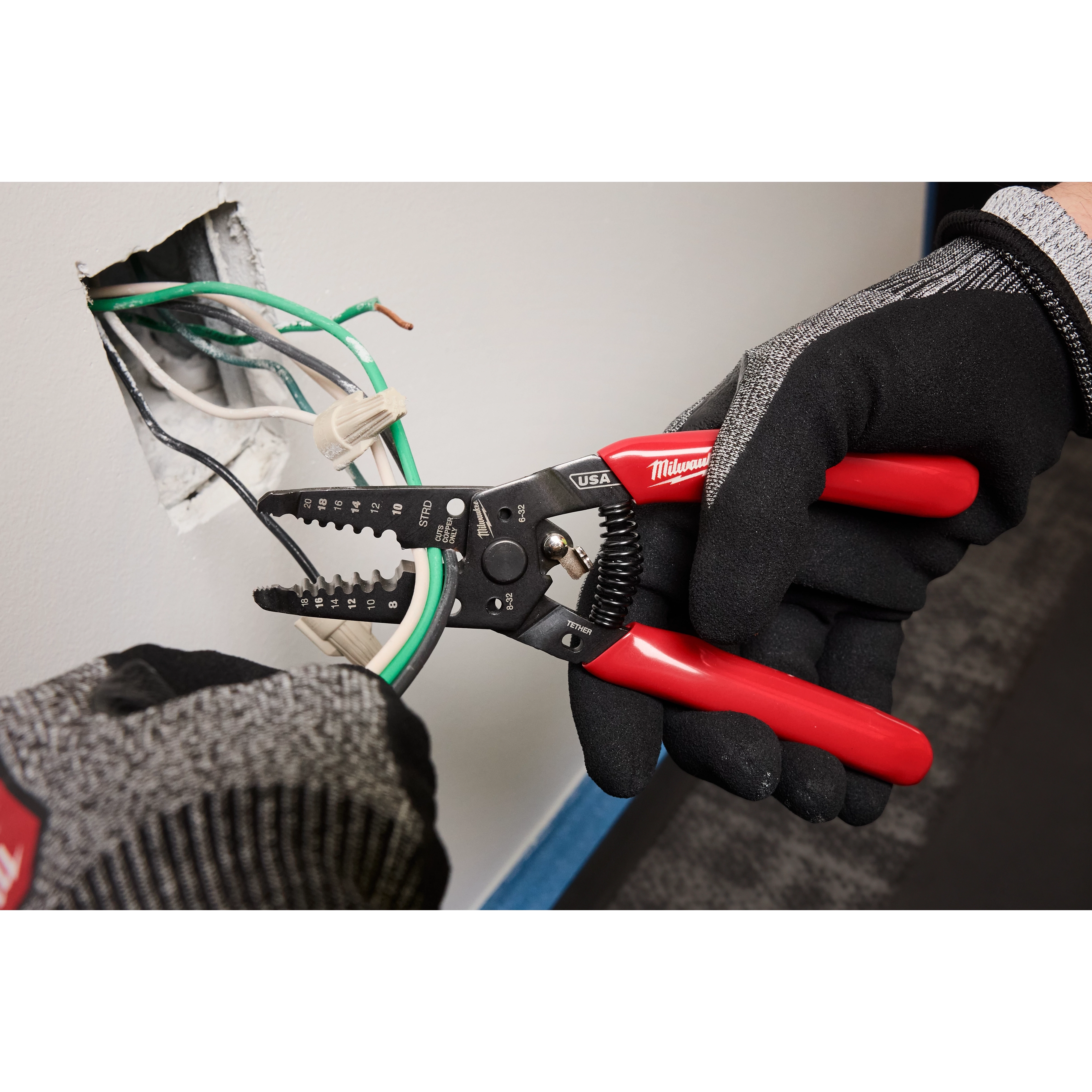 8-20 AWG Dipped Grip Wire Stripper %26 Cutter (USA) used by gloved hands to strip wires from a wall outlet.