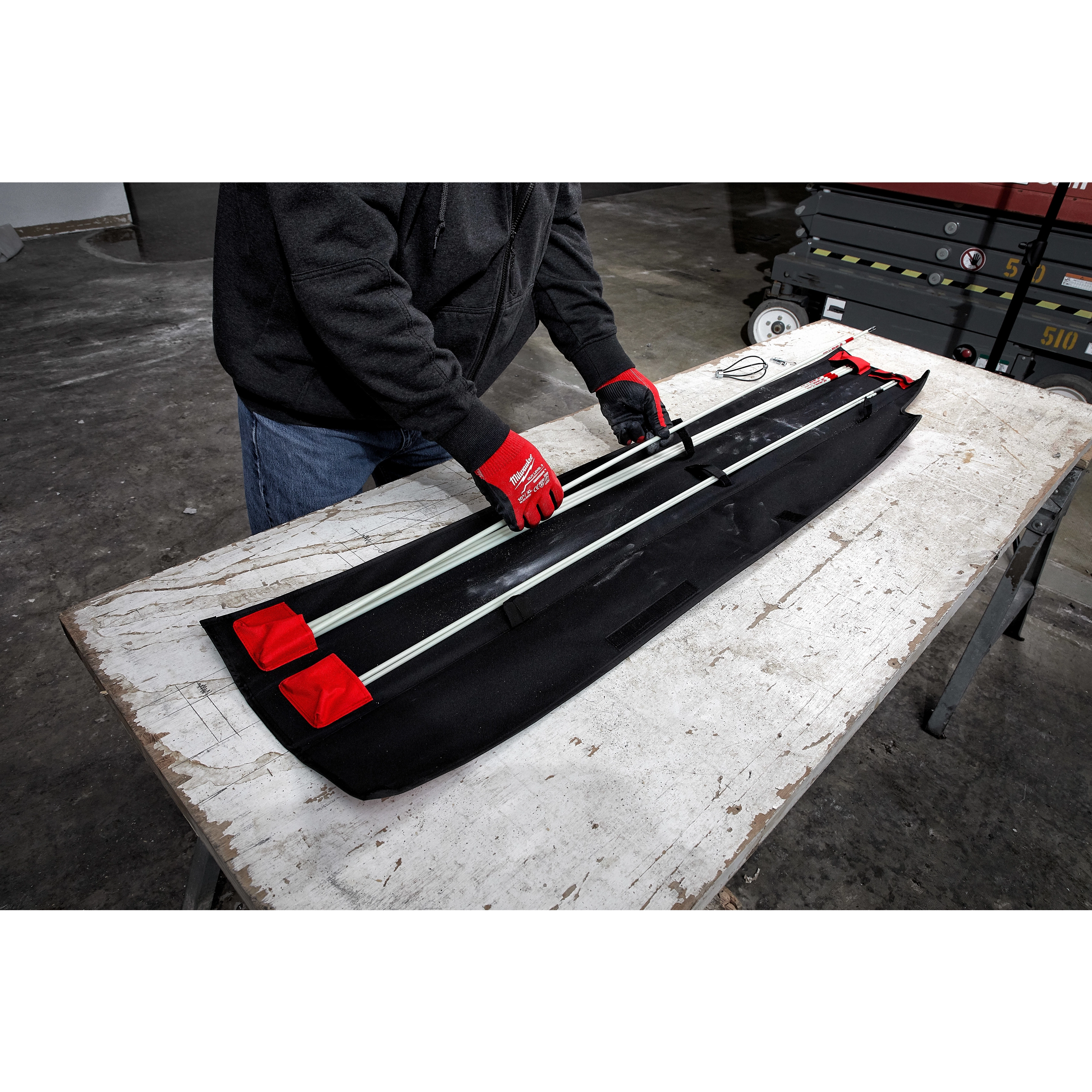 Person assembling a 30%27%20Combo%20Fish%20Stick%20Kit on a table, wearing red gloves. Kit includes several stick rods and a black fabric case.