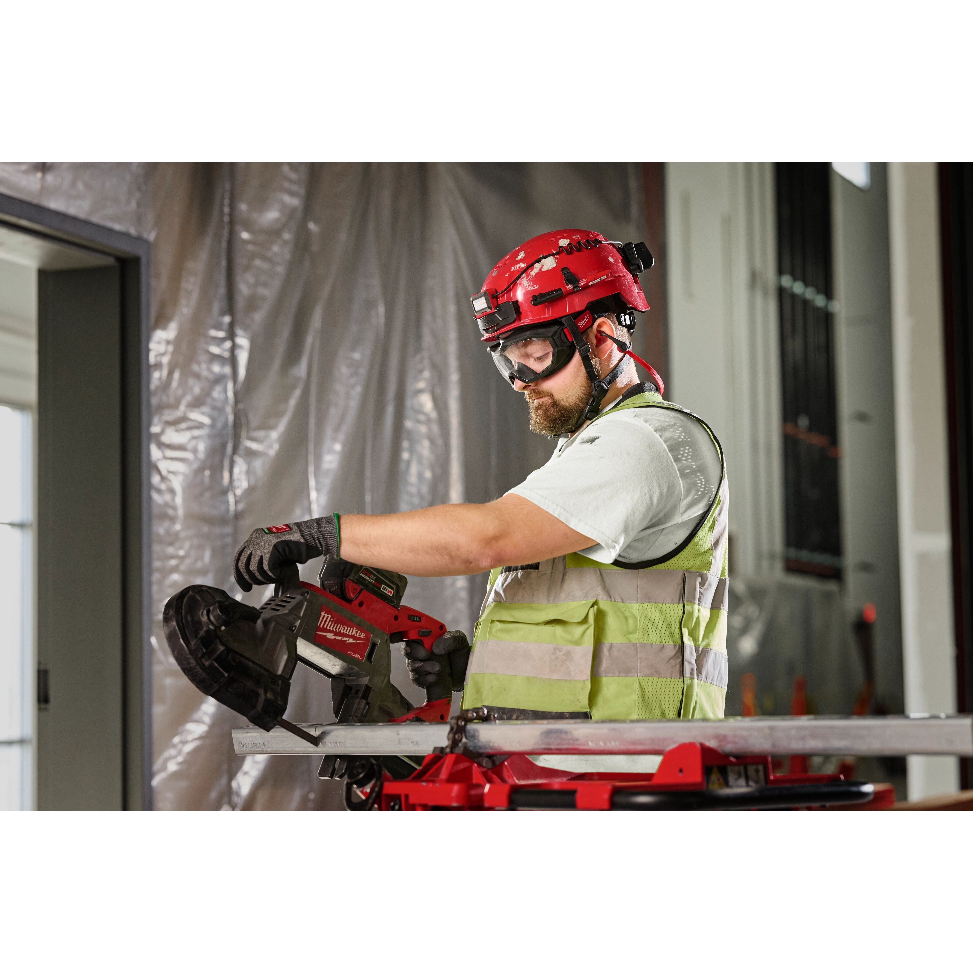A construction worker wearing Vented Goggles - Clear Dual Coat Lens uses a red and black power tool while wearing protective gear.