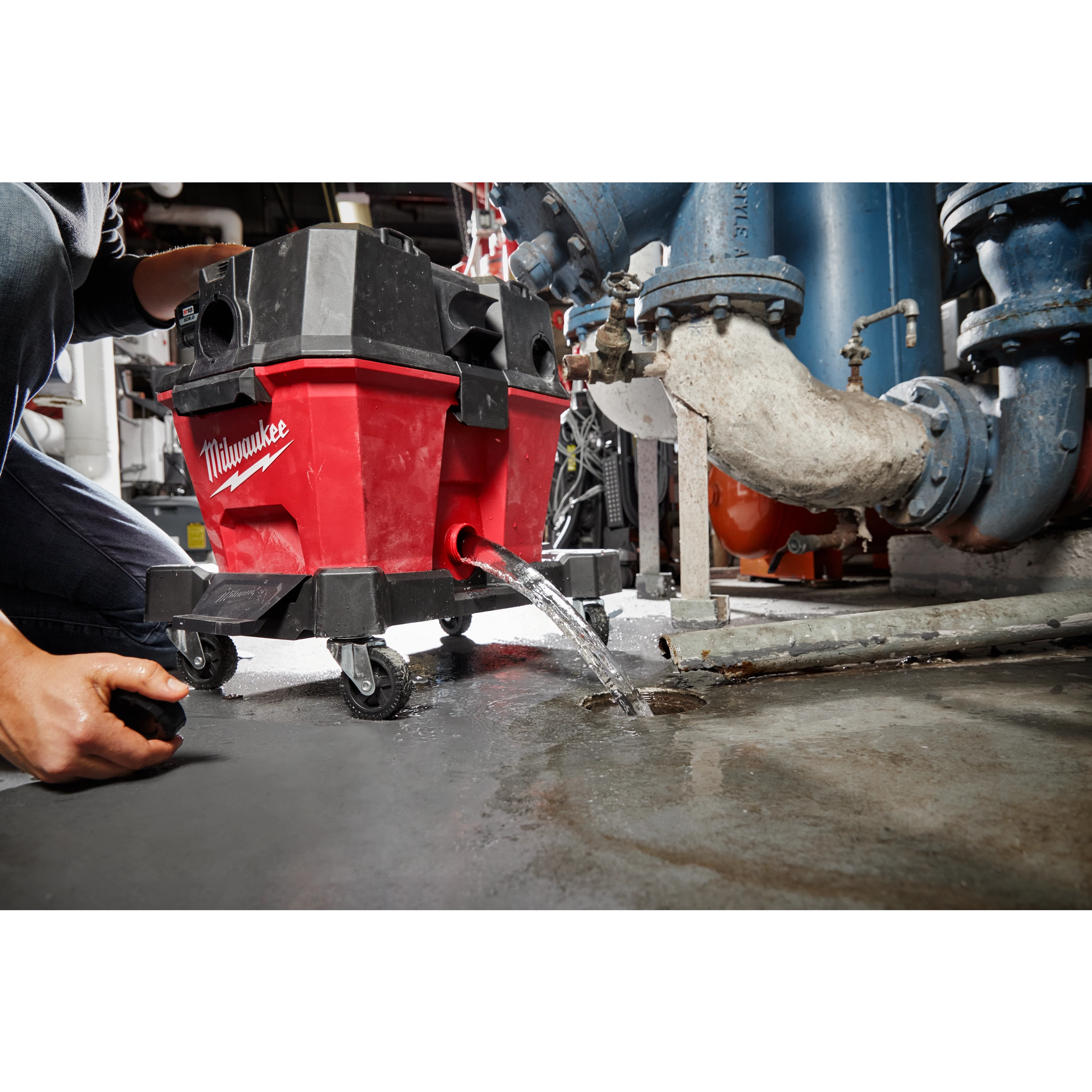 6 Gallon Wet/Dry Vacuum Tank draining water on a concrete floor. A person is kneeling beside the vacuum in an industrial setting.