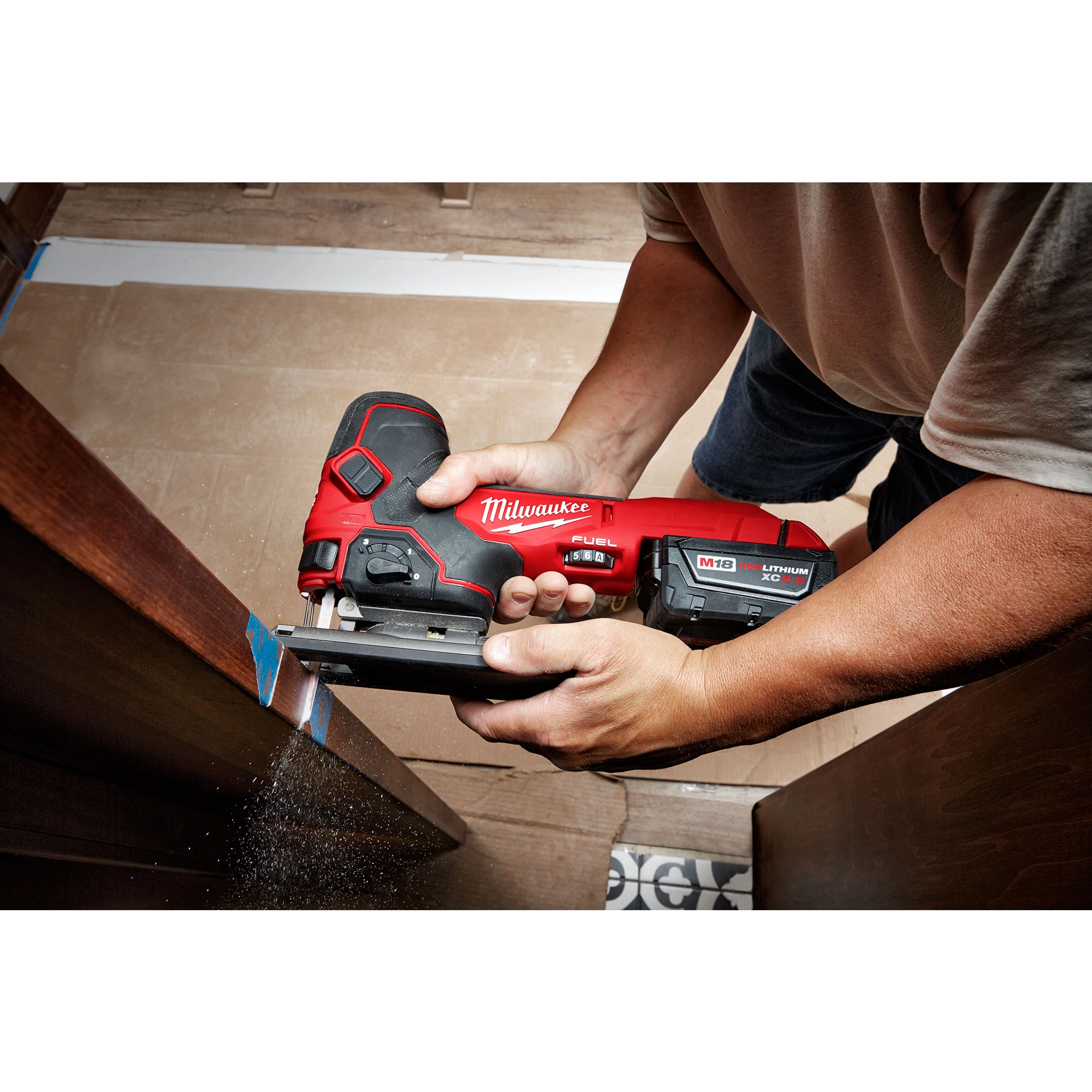 A person uses the Milwaukee M18 Fuel Jigsaw, Barrel Grip to cut wood. The red and black cordless jigsaw features an M18 lithium-ion battery and ergonomic design, providing precise control for detailed work. Dust and wood particles are visible as the tool operates.