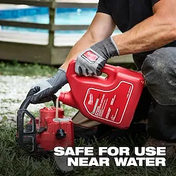 A person in work gloves and pants is pouring Biodegradable All Season Bar and Chain Lubricant from a large red container into a chainsaw's oil reservoir. The text on the image reads, "Safe for use near water." A blurred background includes a pool and wooden deck.