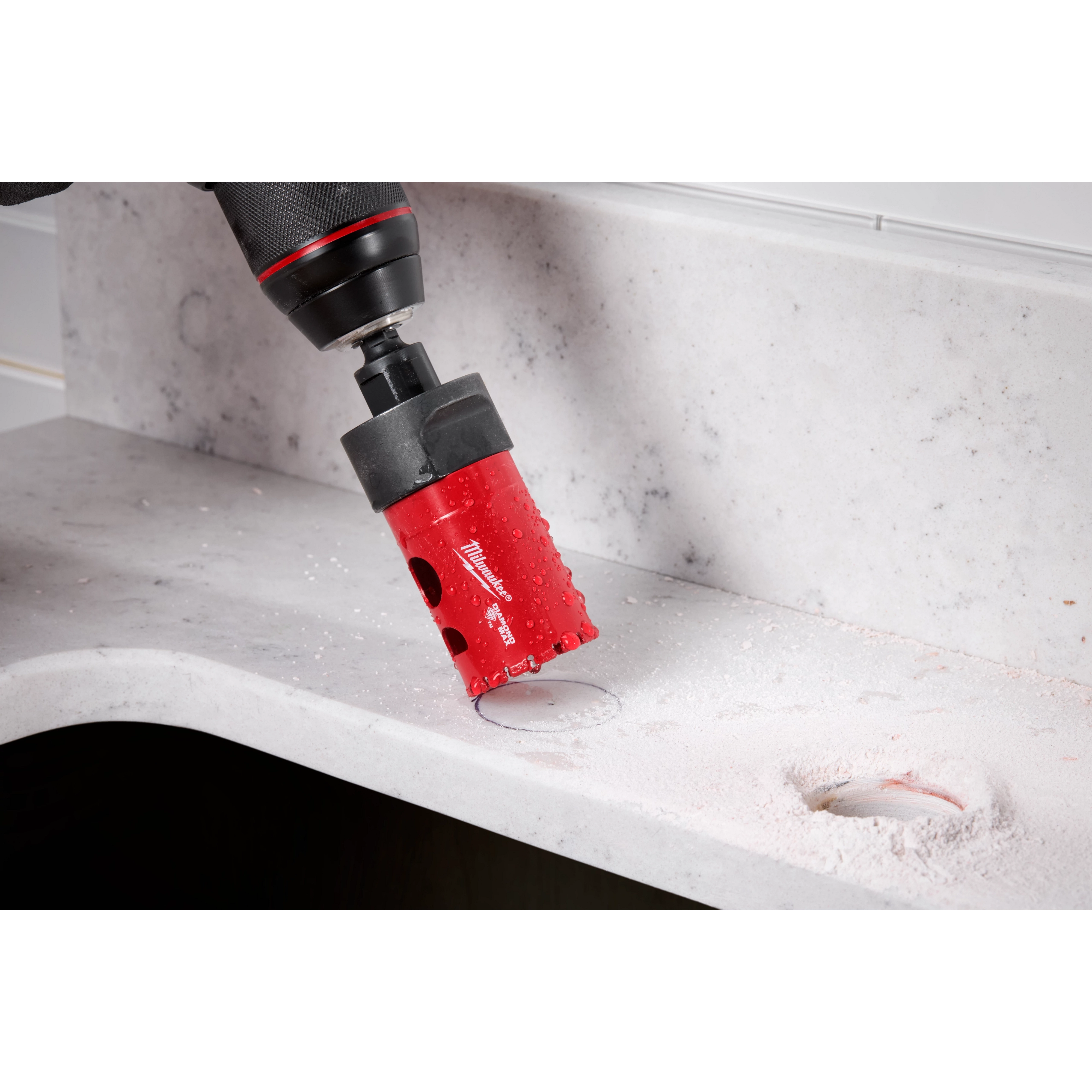 A Milwaukee® 1-3/8" DIAMOND MAX™ Hole Saw attached to a drill is seen cutting through a light gray, stone-like surface. Dust and residue from the cutting are visible around the freshly made hole. Both the tool and the work surface are clearly displayed.