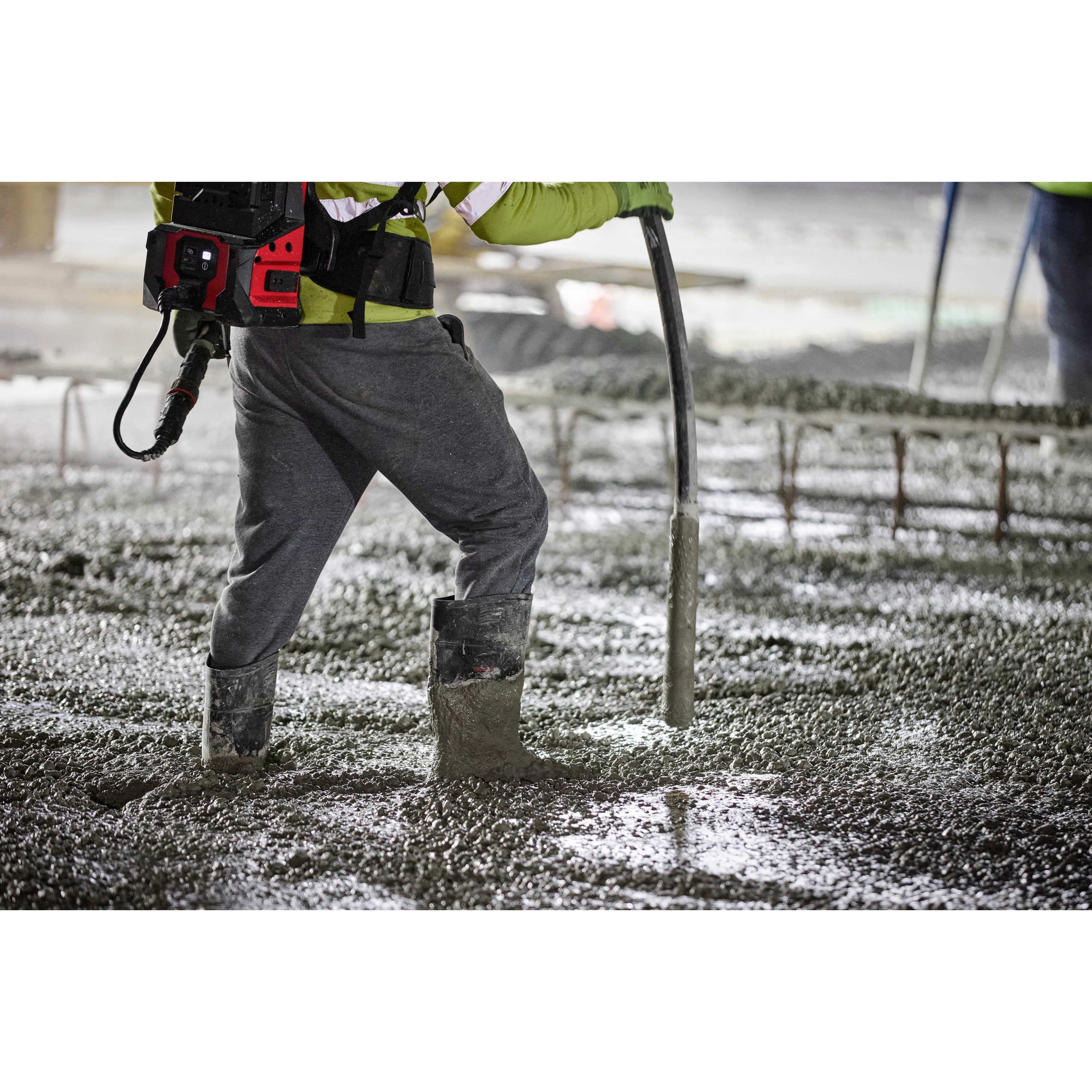 A worker operates an MX Fuel High Cycle Concrete Vibrator on a wet concrete surface, wearing safety gear and boots.