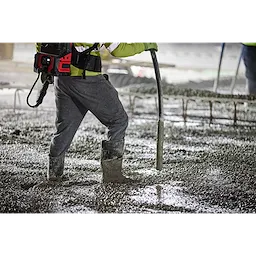 A worker operates an MX Fuel High Cycle Concrete Vibrator on a wet concrete surface, wearing safety gear and boots.