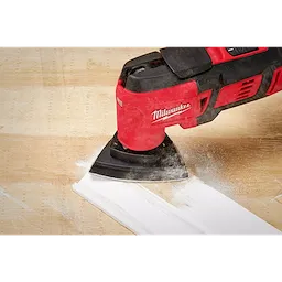 Milwaukee OMT Blades, 3-1/2" Triangle Sanding Pad in use on a wooden surface, creating white dust while smoothing the edge.