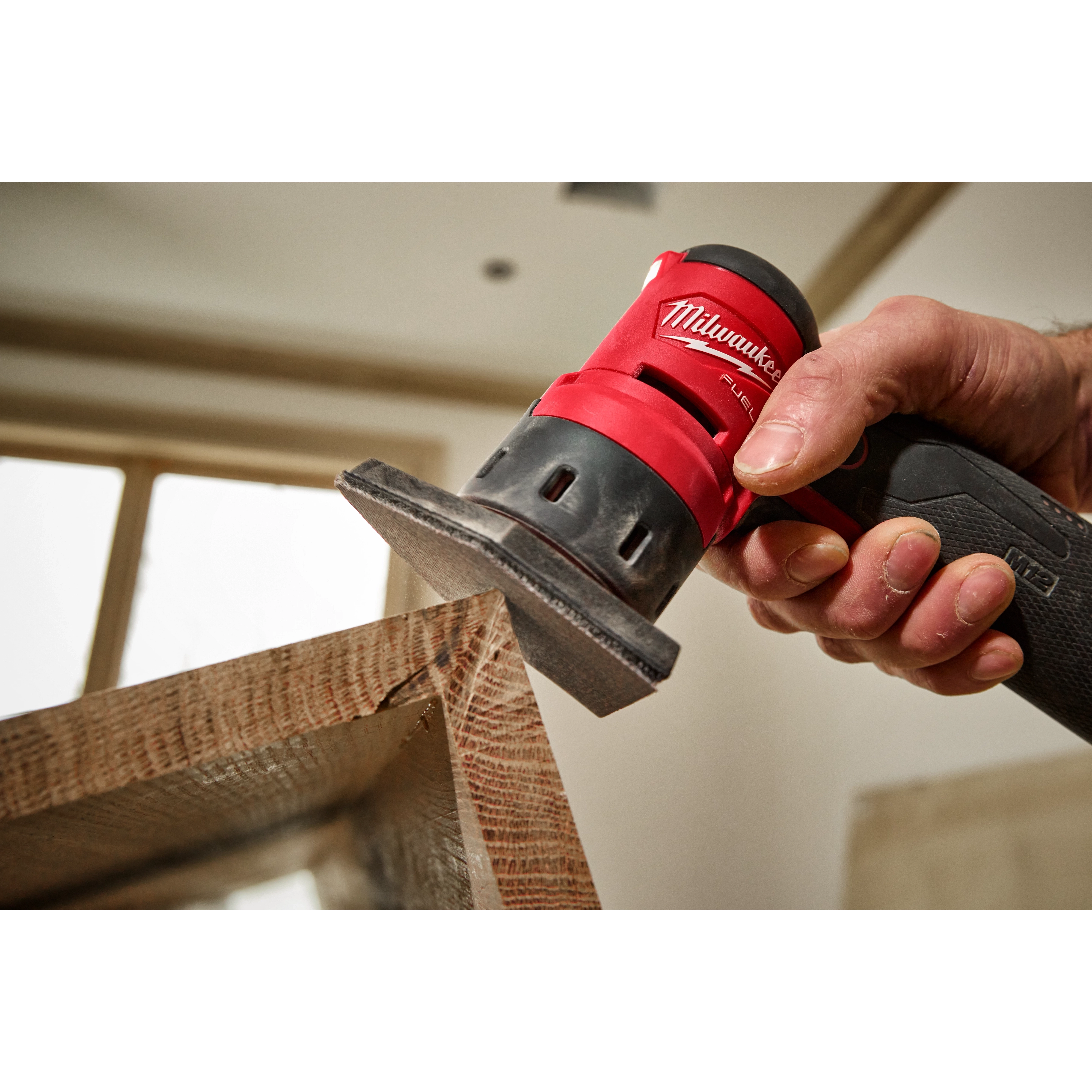 A hand using an M12 FUEL Orbital Detail Sander equipped with 180 Grit Mesh Sanding Sheets to smooth a wooden surface.