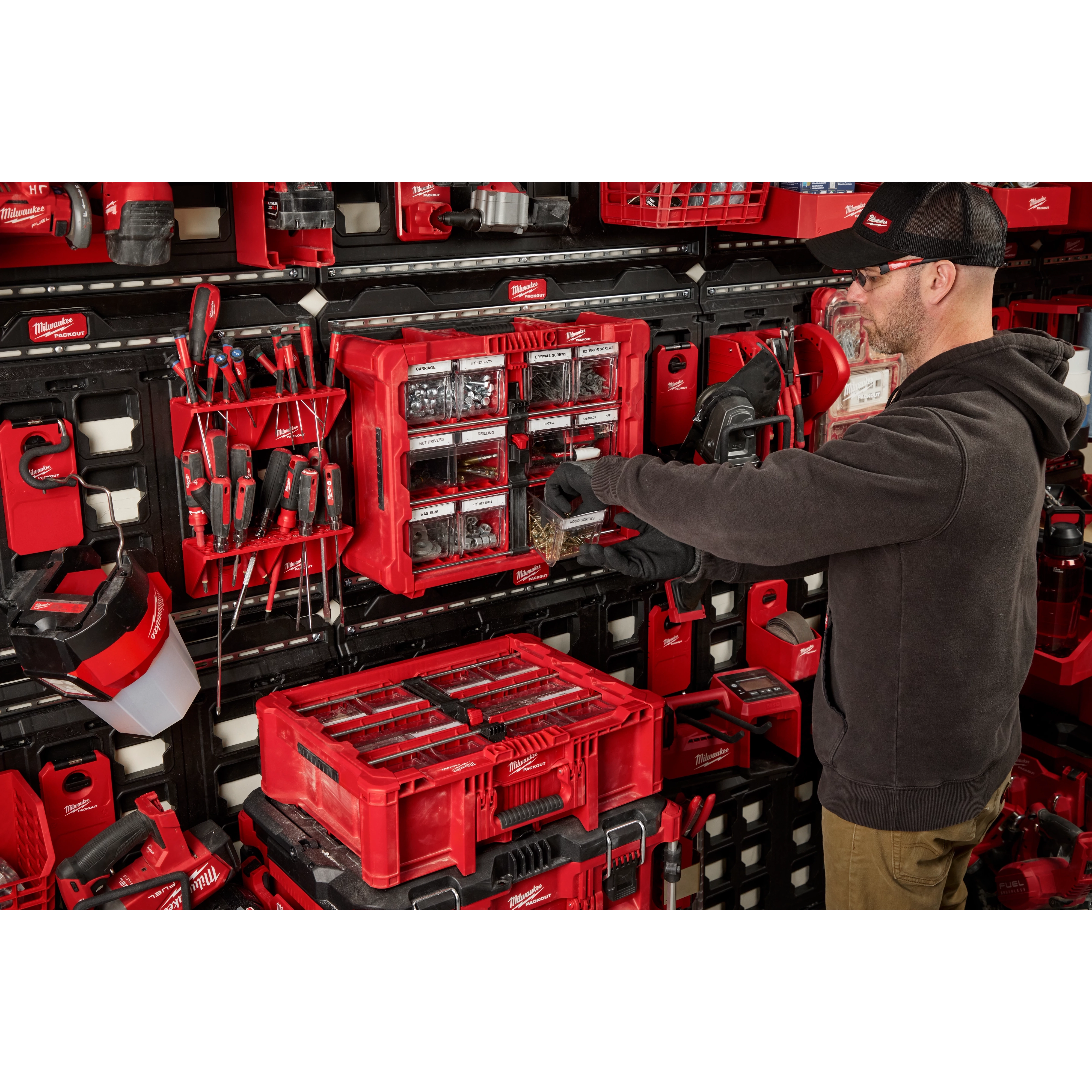 Milwaukee 48-22-8433 PACKOUT Tilt Bin Organizer mounted on a PACKOUT wall setup holding labeled hardware bins in a workshop storage area