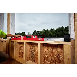 Person using a 48"-78" Expandable Install Level to measure the levelness of a wooden frame in an outdoor construction setting.