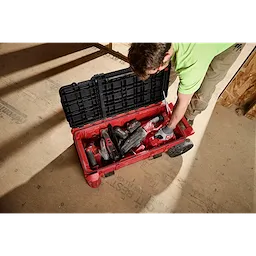 Worker reaching into PACKOUT Compact Rolling Tool Chest filled with power tools on a construction floor.
