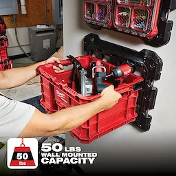 Person mounting a red PACKOUT Mounting Plate holding tools, rated for a 50 lbs wall-mounted capacity, onto a wall.