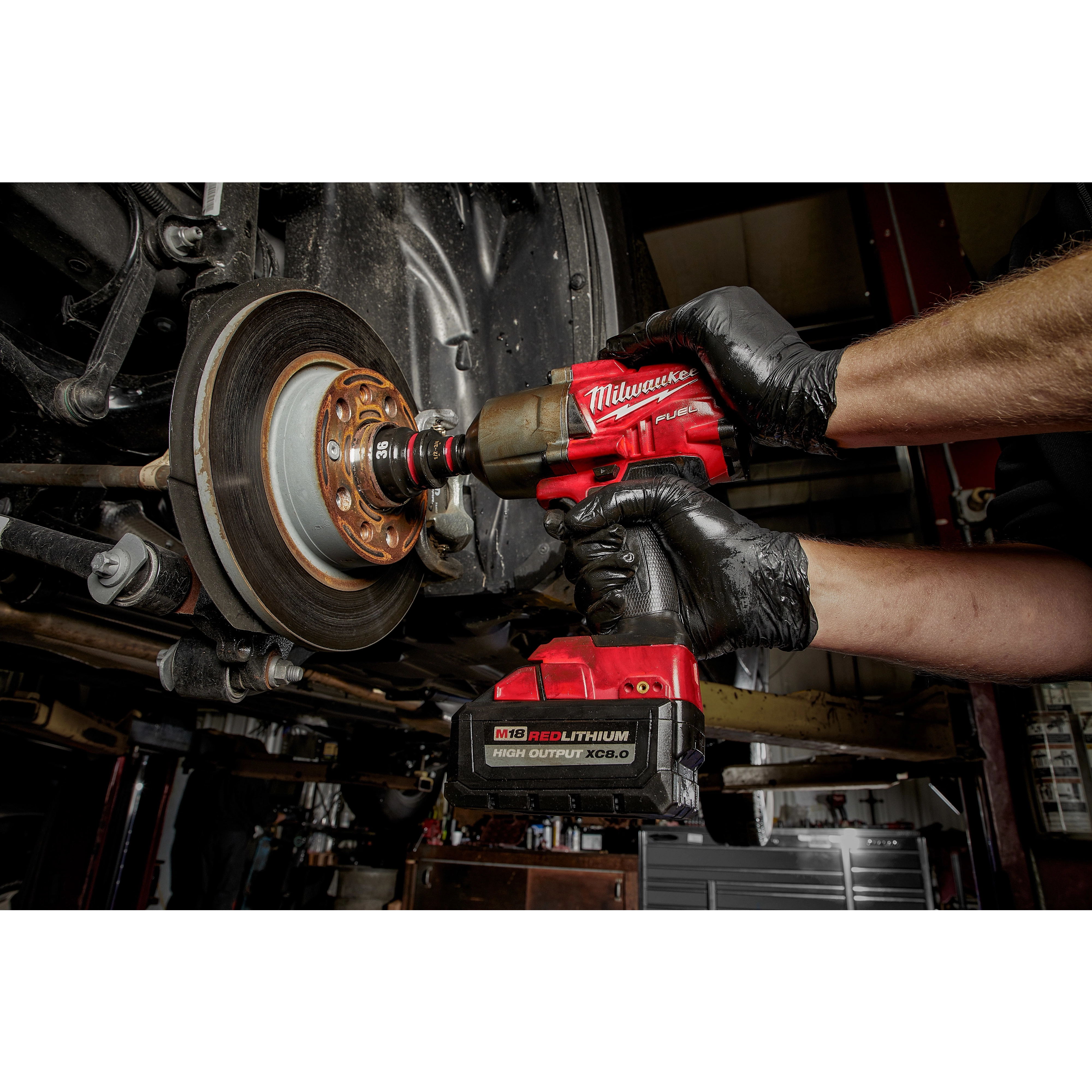 A person uses the SHOCKWAVE Impact Duty 3/4" Drive 36MM Deep 6 Point Socket and a red impact wrench to work on a vehicle's wheel assembly.