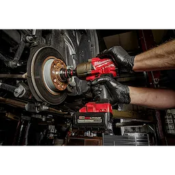 A person uses the SHOCKWAVE Impact Duty 3/4" Drive 36MM Deep 6 Point Socket and a red impact wrench to work on a vehicle's wheel assembly.