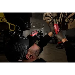 A mechanic works on a vehicle with a Milwaukee Rechargeable Clip Light attached to his cap for illumination.