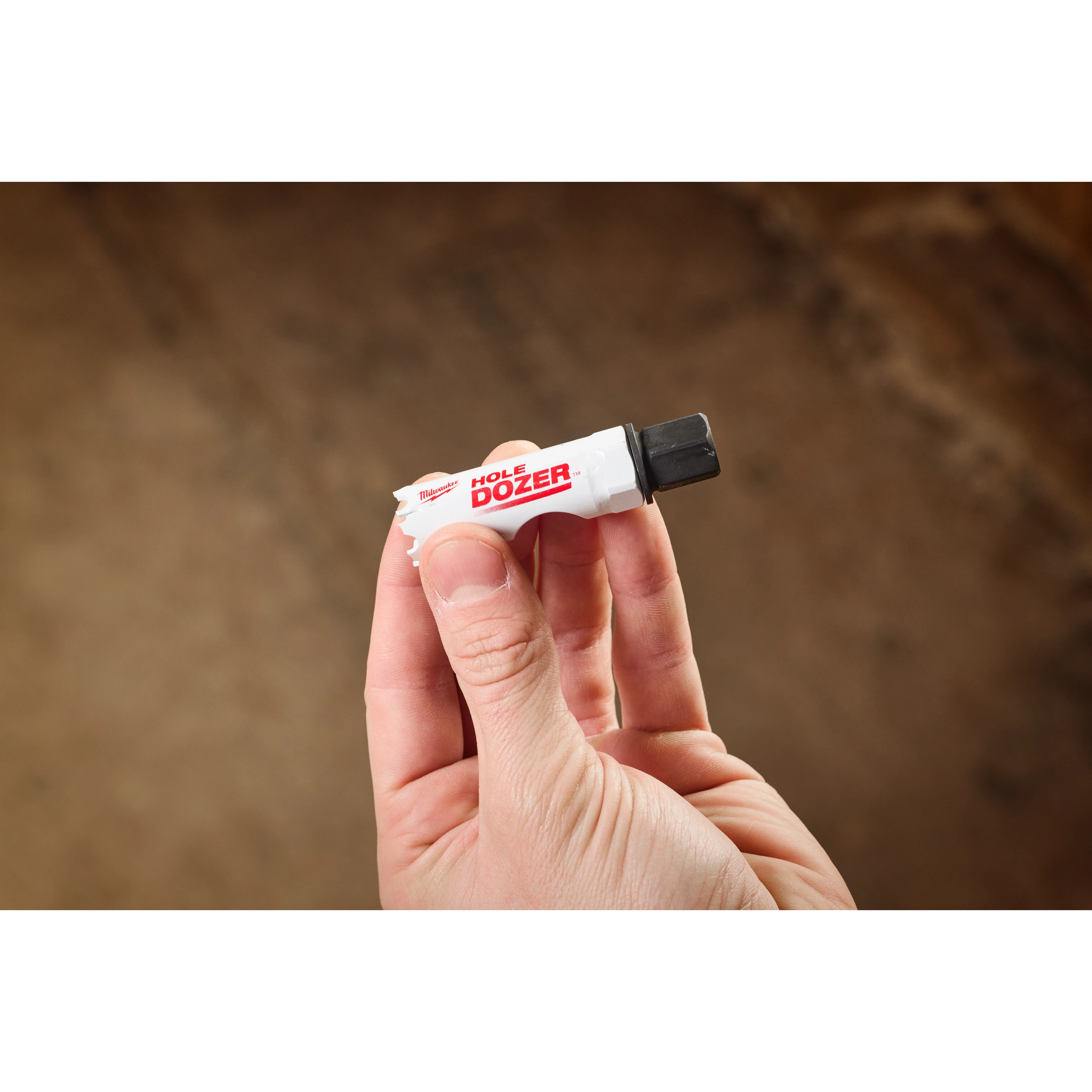 A hand holds a 5PK Small Adapter for QUIK-LOK™ Arbor. The adapter is white with red "HOLE DOZER" text and features a metal end for attaching to drilling equipment.