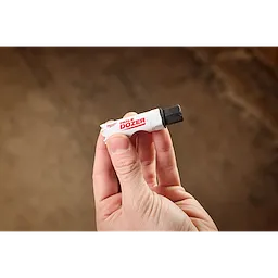 A hand holds a 5PK Small Adapter for QUIK-LOK™ Arbor. The adapter is white with red "HOLE DOZER" text and features a metal end for attaching to drilling equipment.